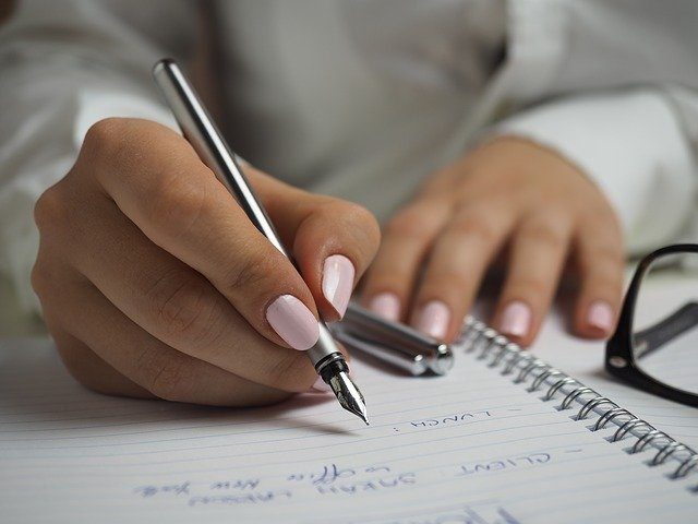 Woman writing, notebook, pen, stay motivated